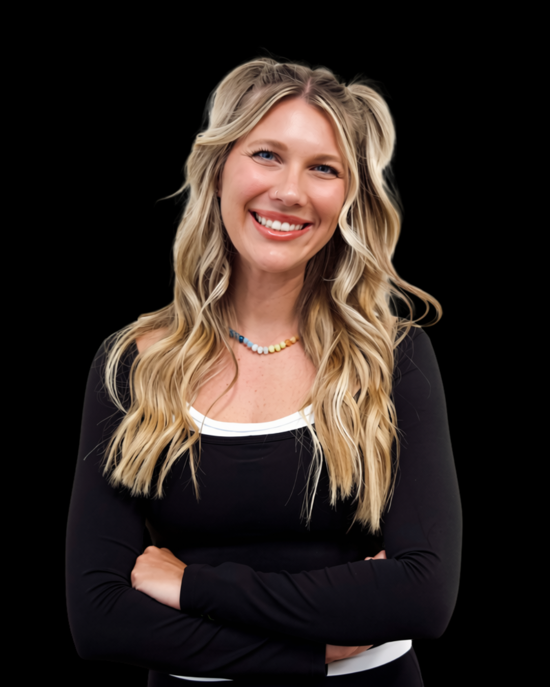 A woman with long, wavy blonde hair smiling, wearing a black top and a colorful beaded necklace, standing with arms crossed against a black background.