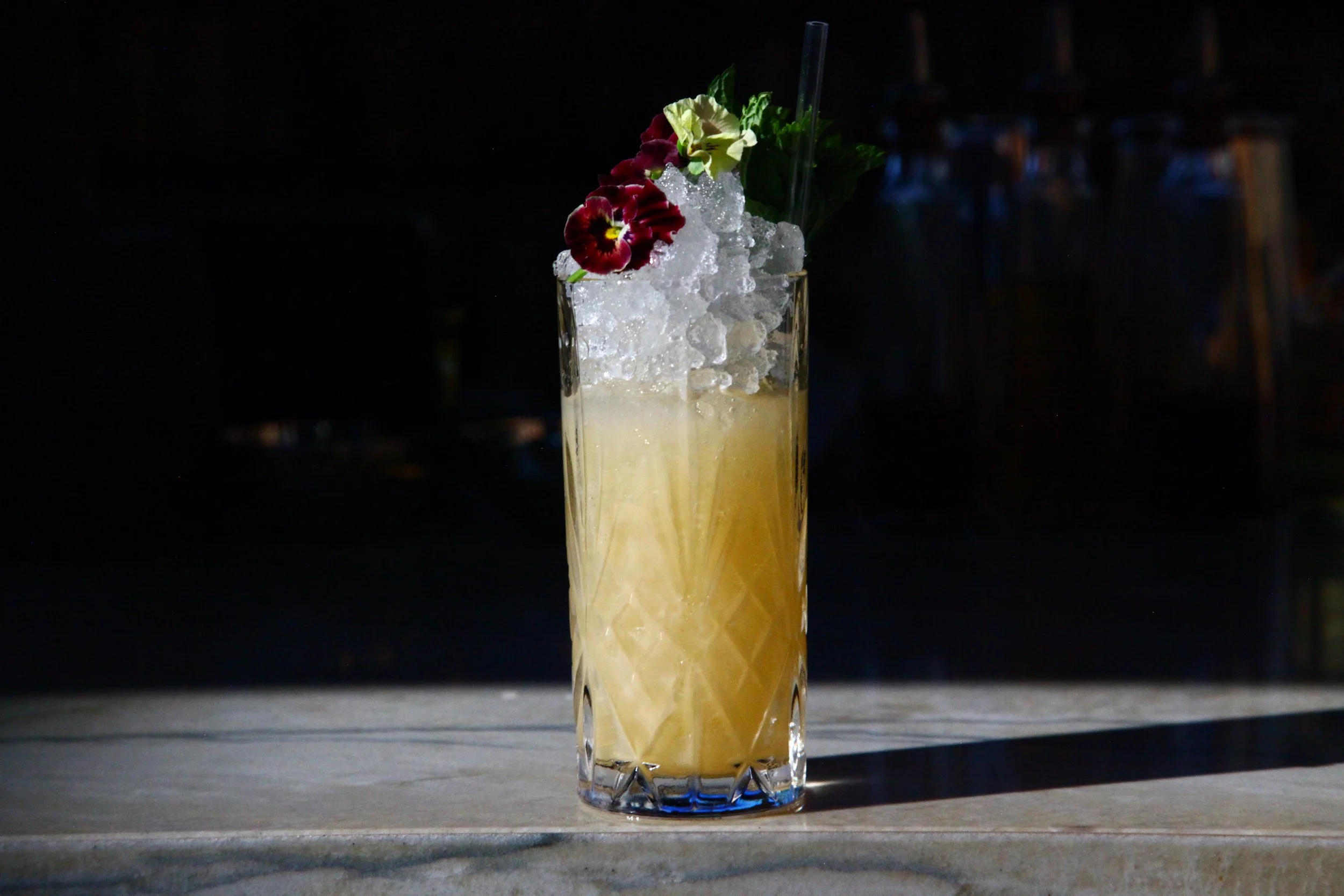 Pineapple craft cocktail served at Vici Rooftop, garnished with fresh mint, citrus, and flowers