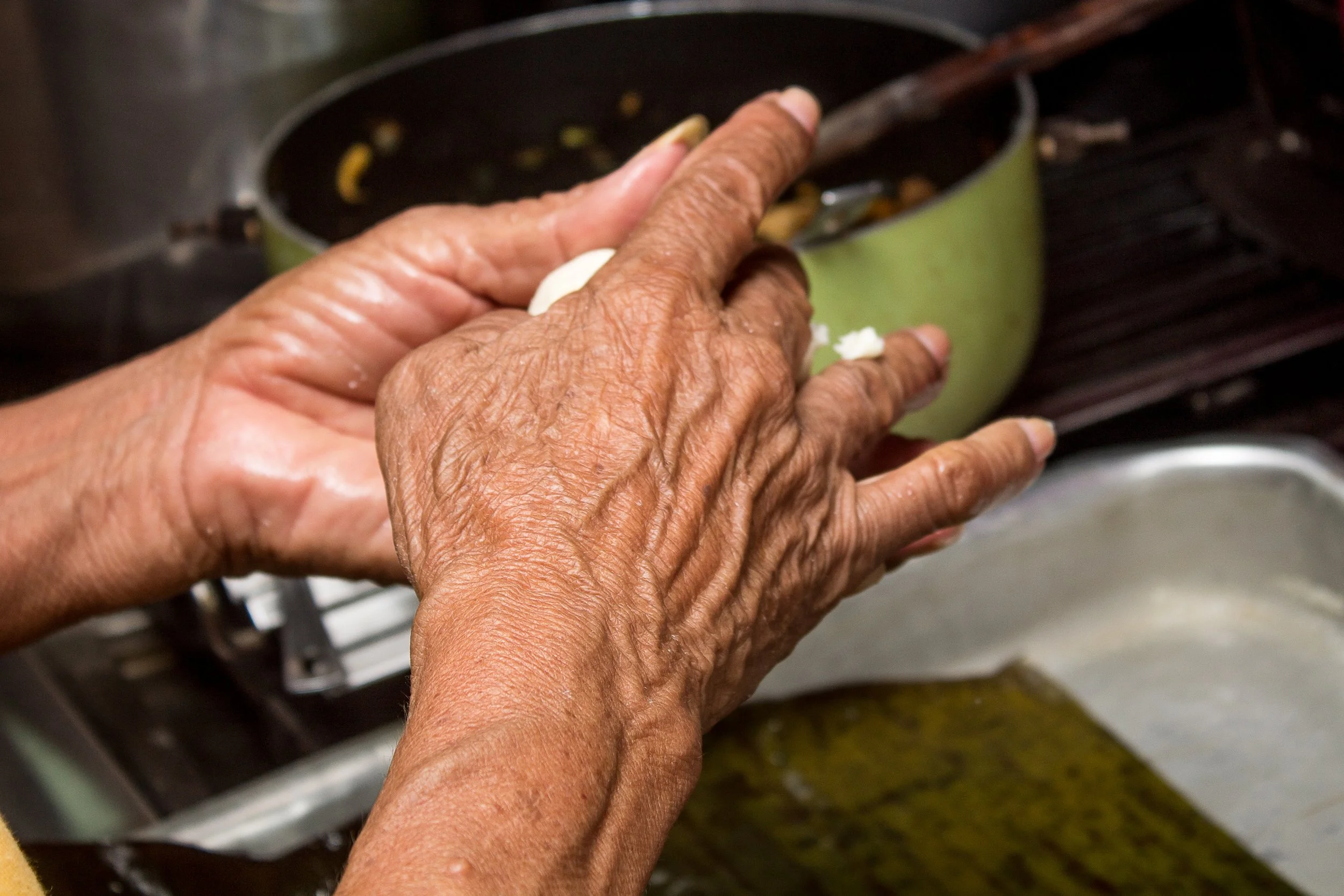 An older woman’s hands preparing food over a kitchen sink.