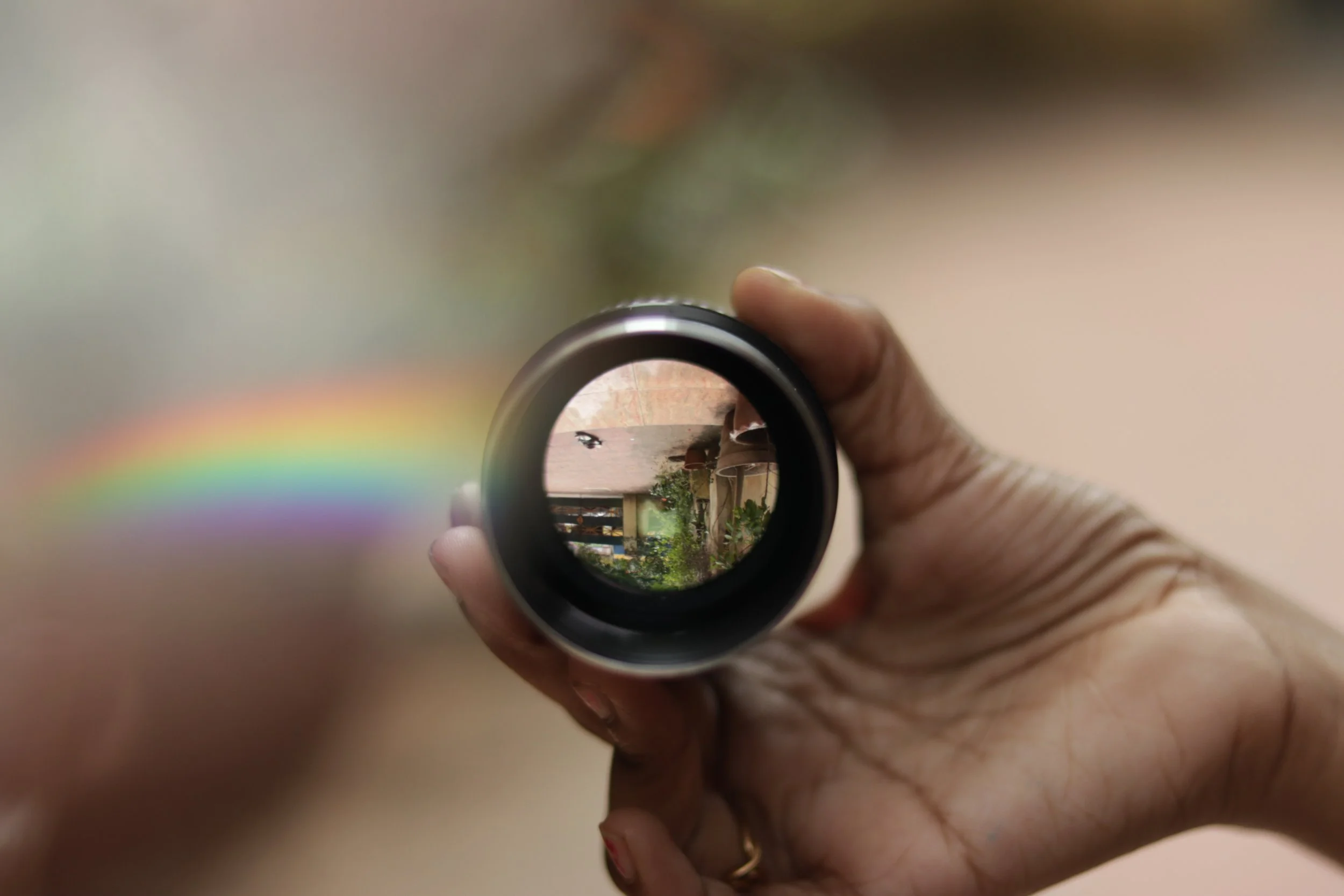 A hand holding a small lens that refracts a rainbow across the background.