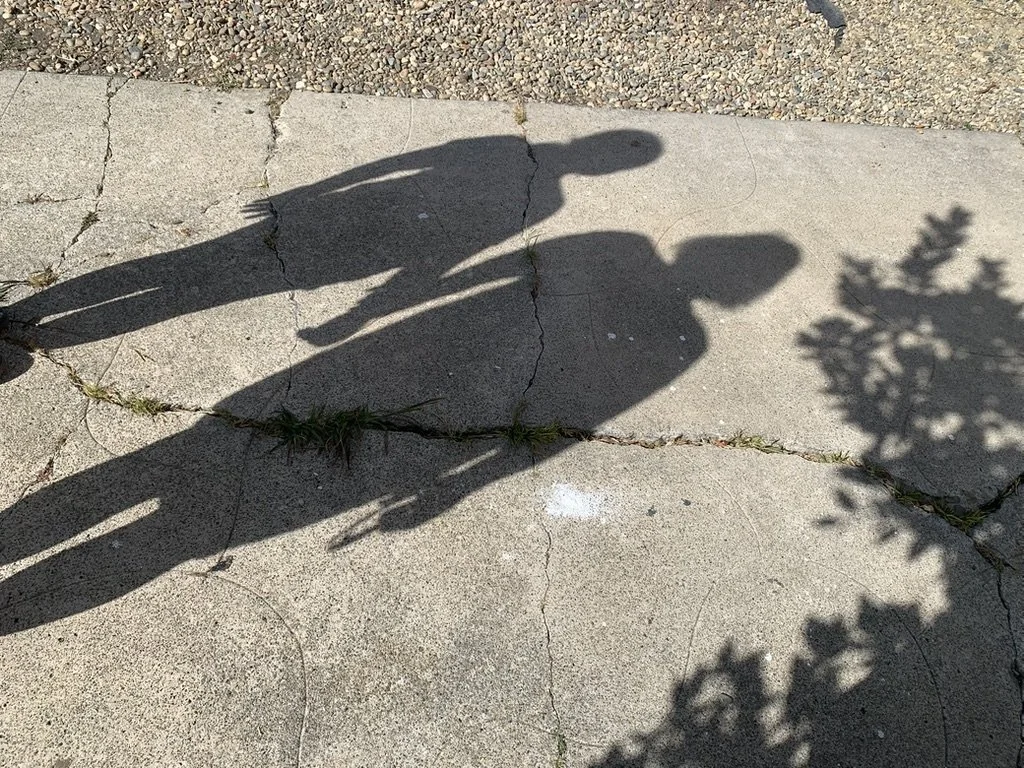 Shadows of Nidia and Ellie holding hands on a sunlit sidewalk.