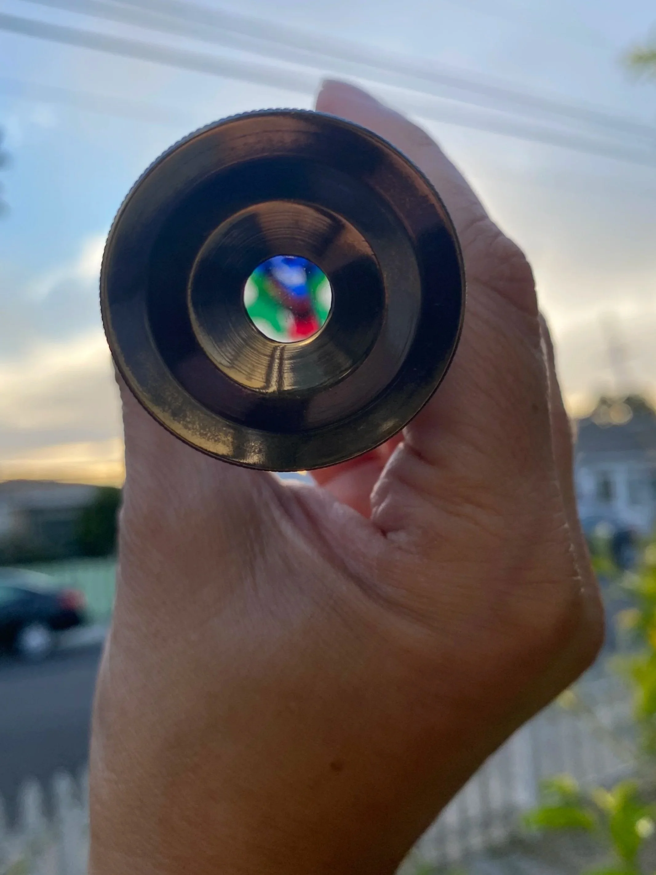 A hand holding a small lens with shifting colors visible through its center.