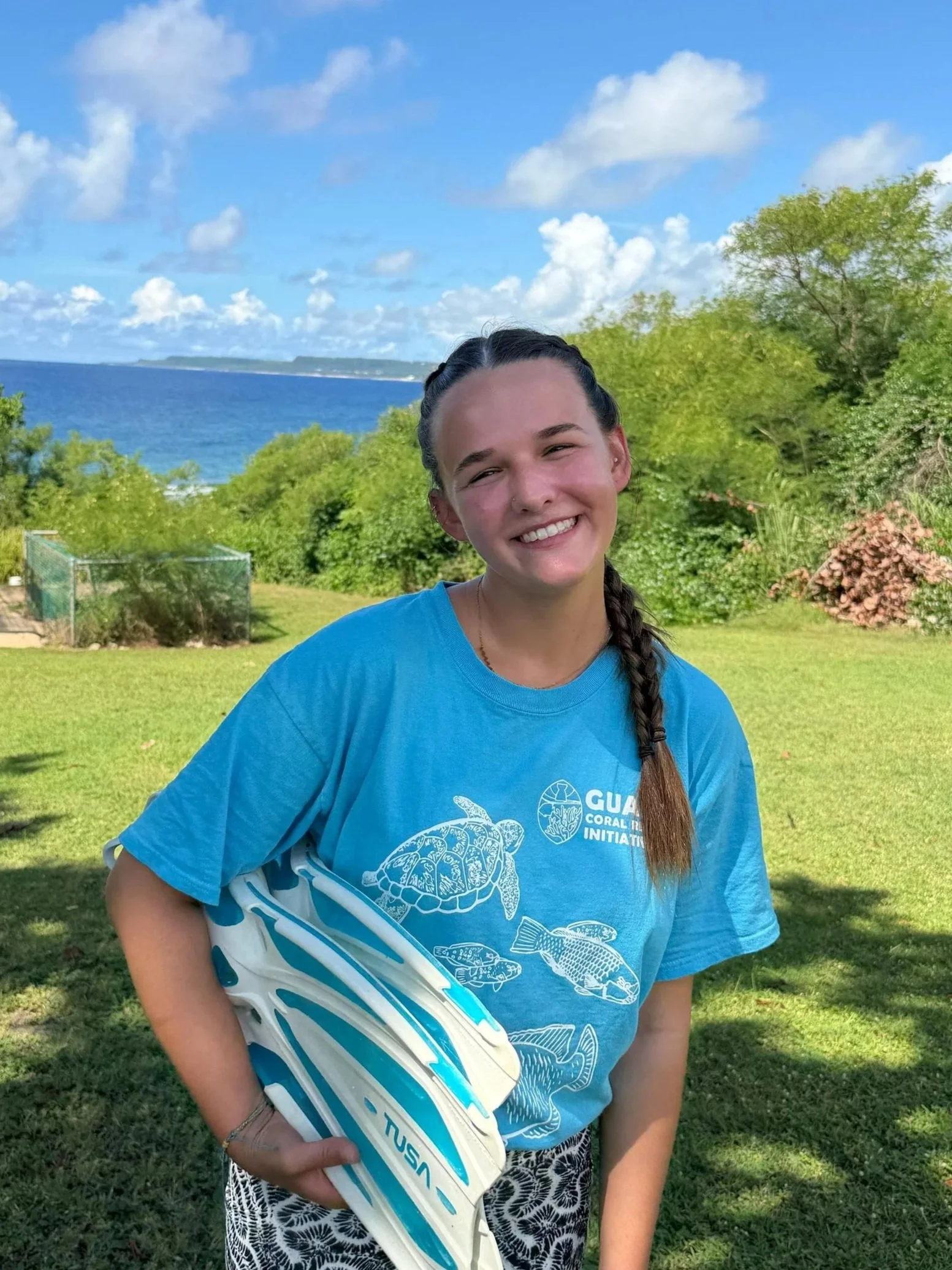 GCRI staff member smiling at the camera with greenery and the ocean in the background
