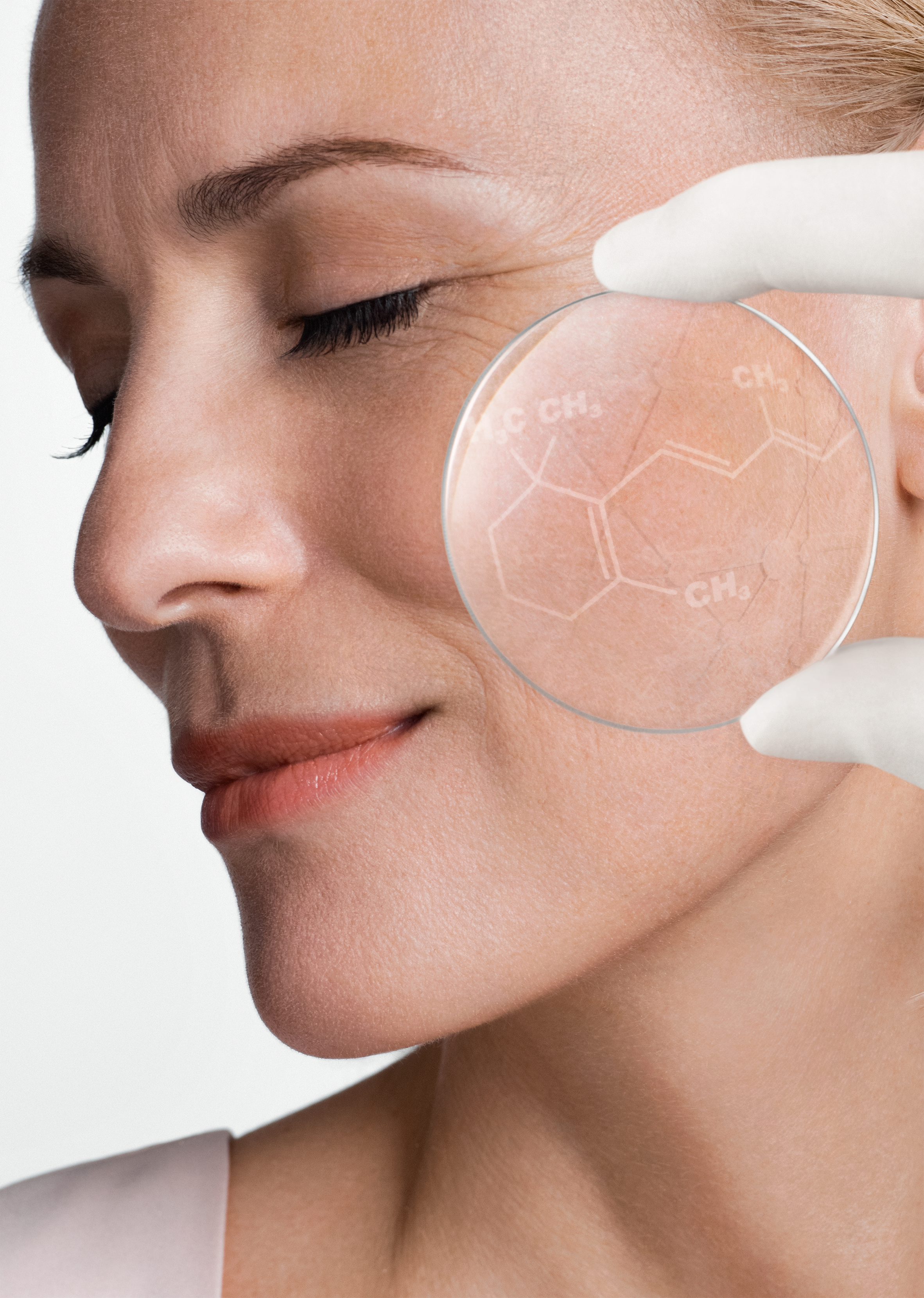 Close-up of a woman with closed eyes, holding a transparent circle with a chemical structure near her cheek, indicating skincare or science.