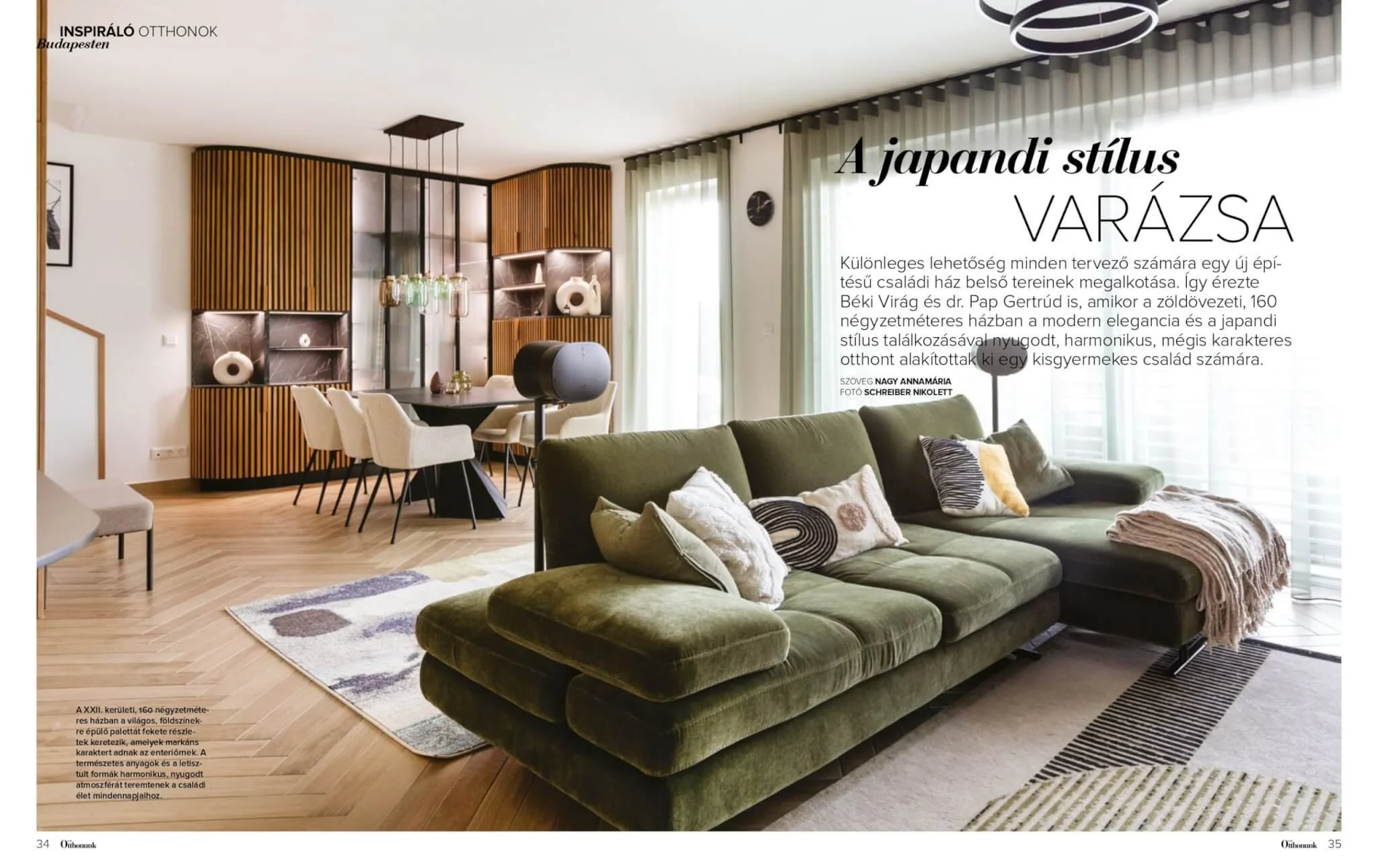Interior of a modern living room with a green velvet sofa, decorative pillows, a beige armchair, a patterned rug, and a wooden dining table with white chairs. There are wooden wall panels, glass-self shelving, a pendant light fixture, along with shee