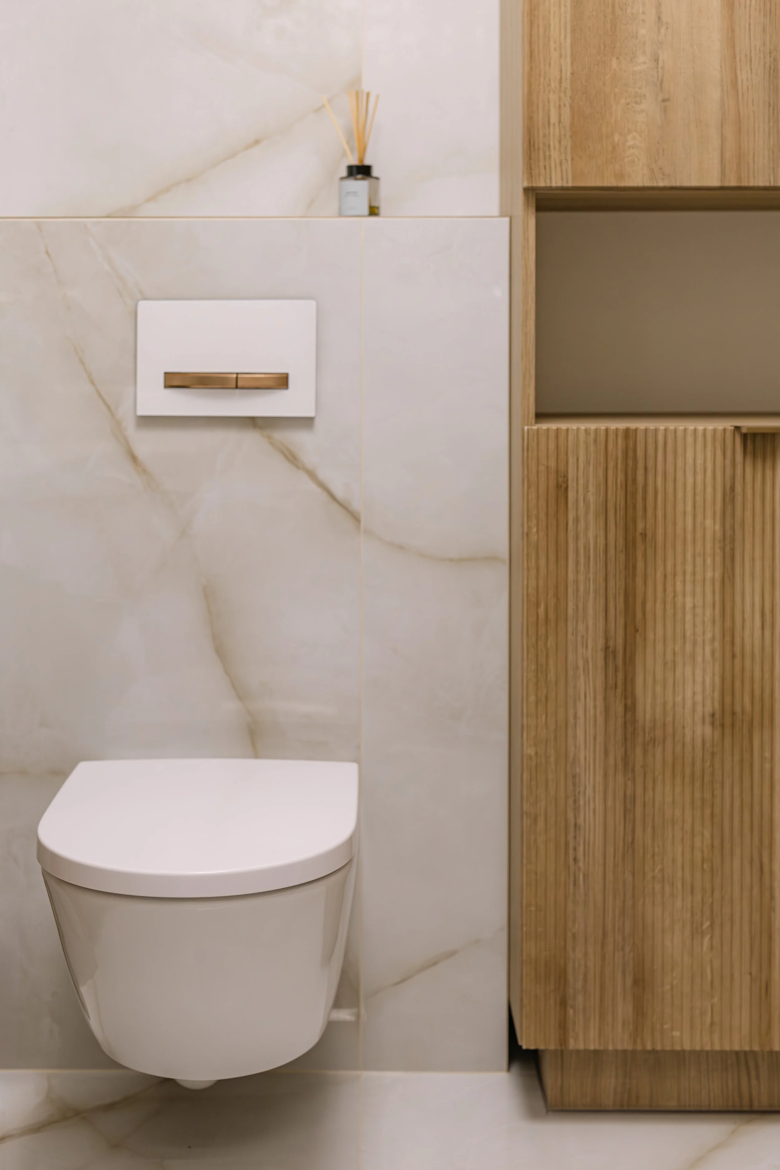 Modern bathroom with a wall-mounted toilet, marble walls, and a wooden cabinet.