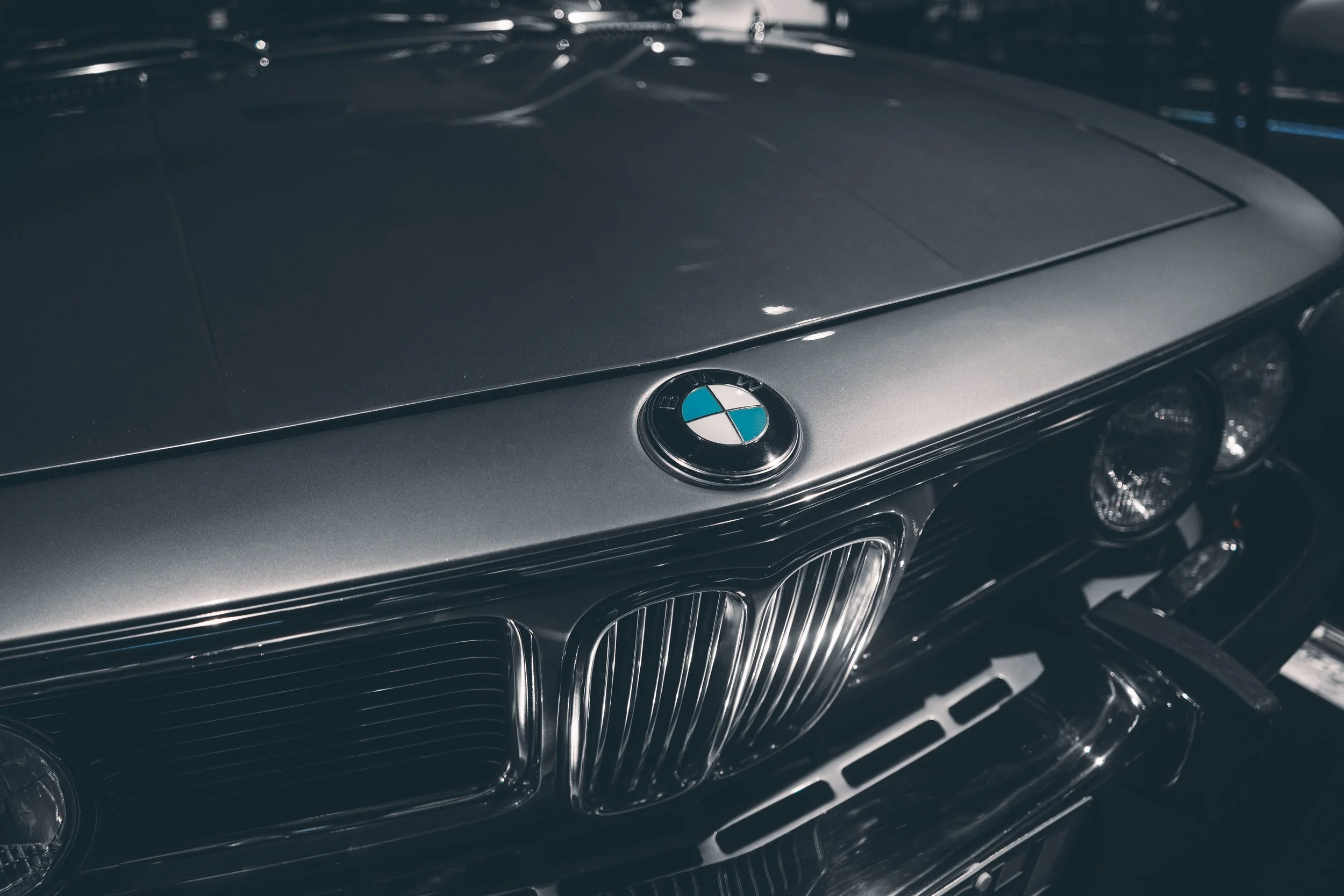 Nærbilde av fronten på en klassisk BMW med grill og sigerringer, i en mørk parkeringshvelv, med BMW-logo på panseret.