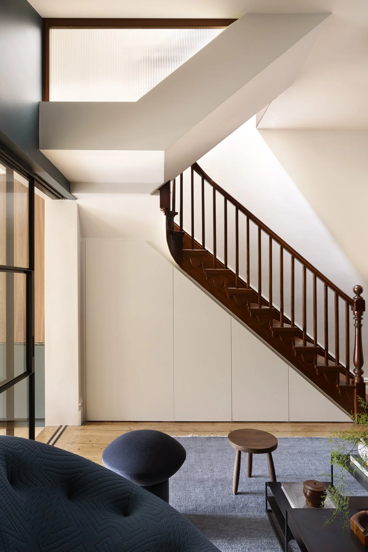 Victorian heritage staircase with new contemporary under stair storage. Blue living room with black steel and glass doors