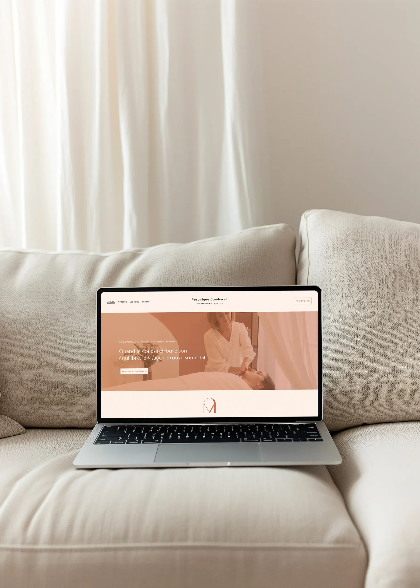 Un ordinateur portable sur un canapé beige avec un écran affichant un site web de réflexologie faciale, dans un salon lumineux avec des rideaux blancs.