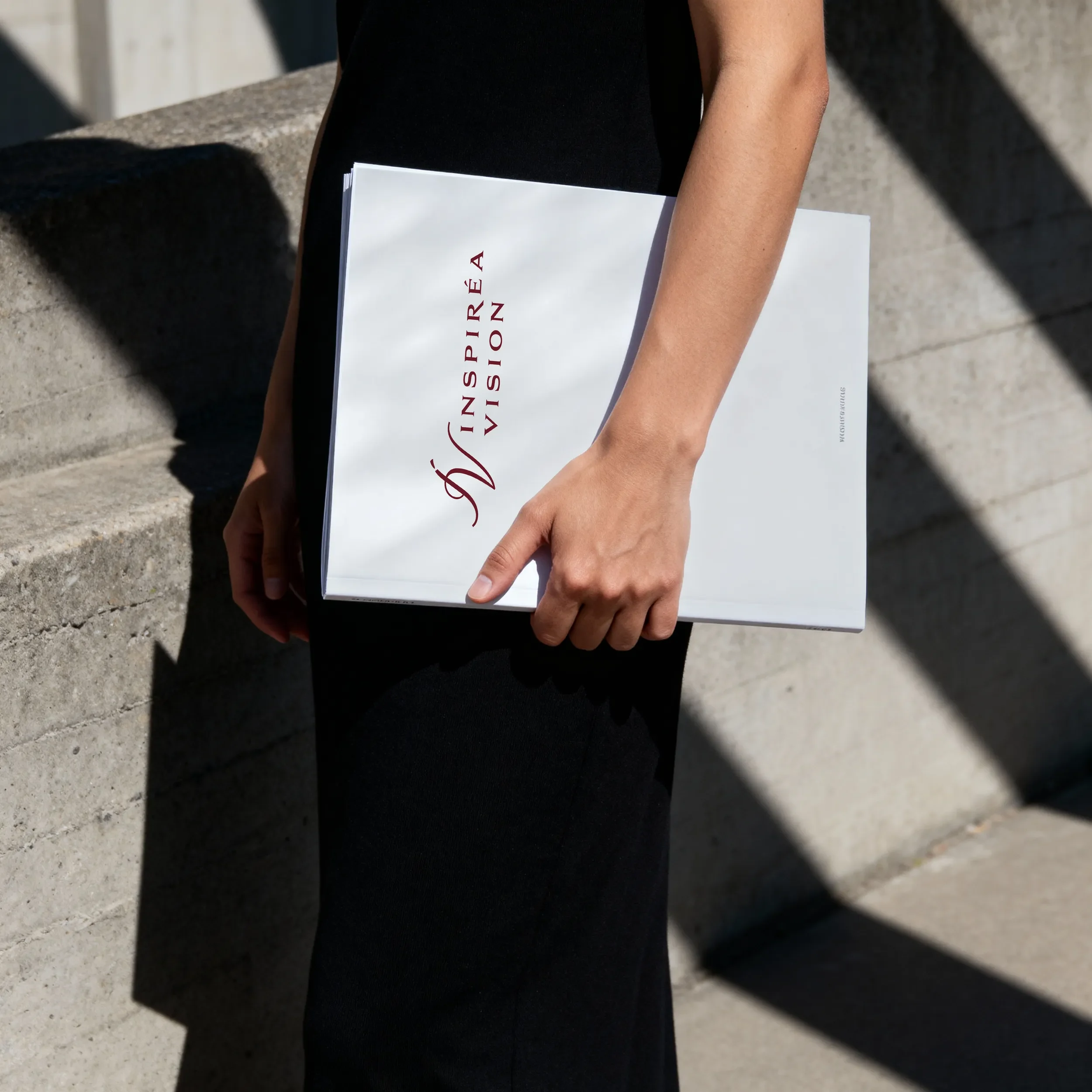Une personne tient un livre blanc avec du texte en rouge et noir dans un environnement extérieur.
