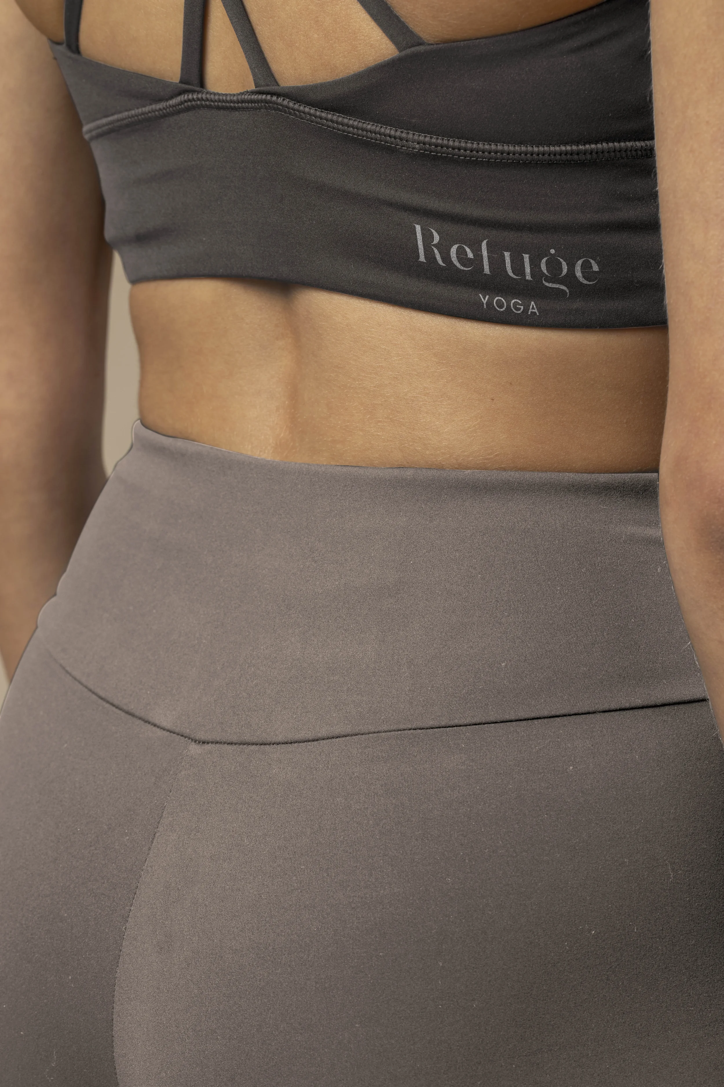 Vente d'un vêtement de sport noir avec le logo 'Refuge YOGA' sur la poitrine, porté par une personne dont la peau est bronzée, avec un pantalon gris et un haut sport.