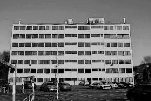 Black and white photo of a multi-story office building with a parking lot in front.