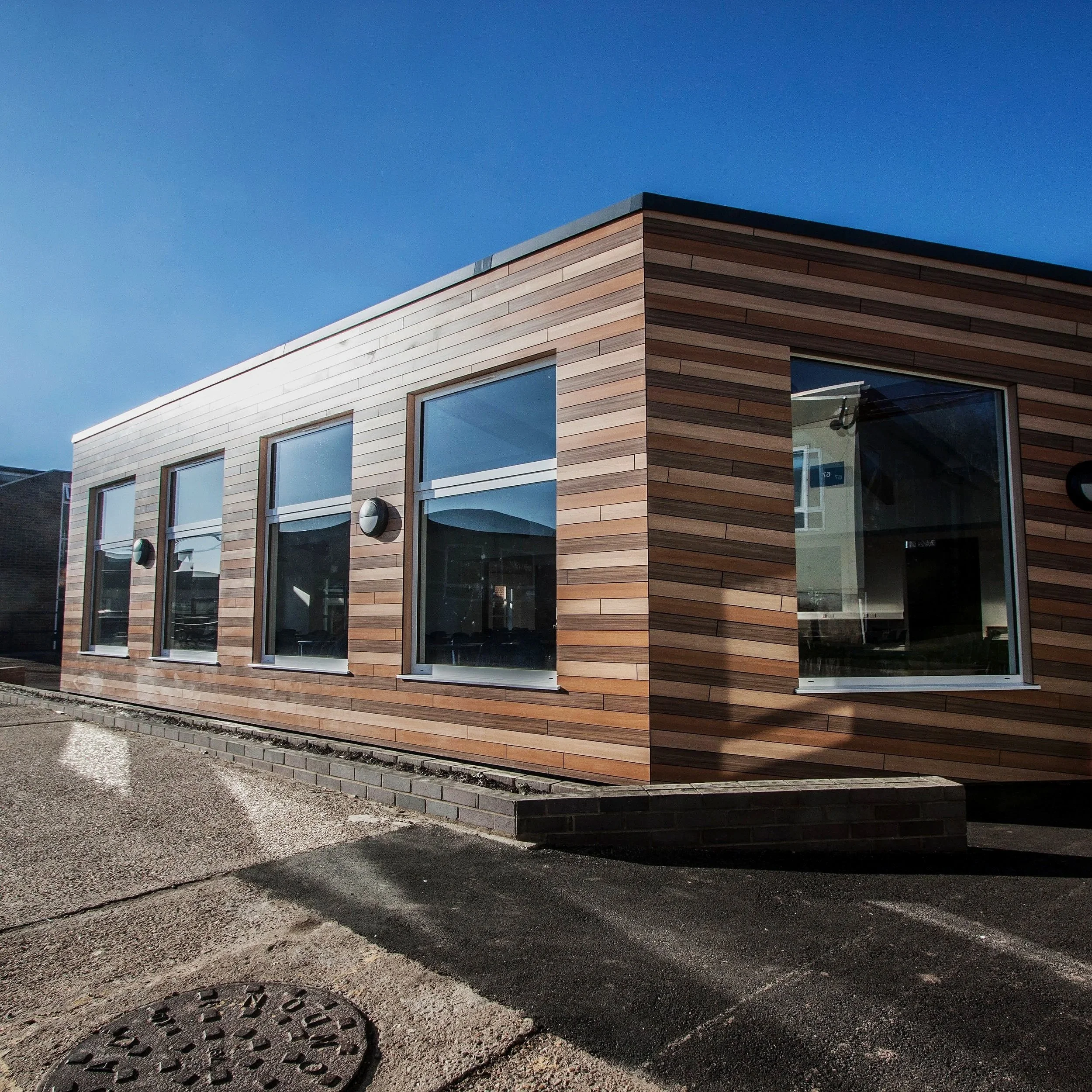 Modern building with wooden exterior and large windows under a clear blue sky.