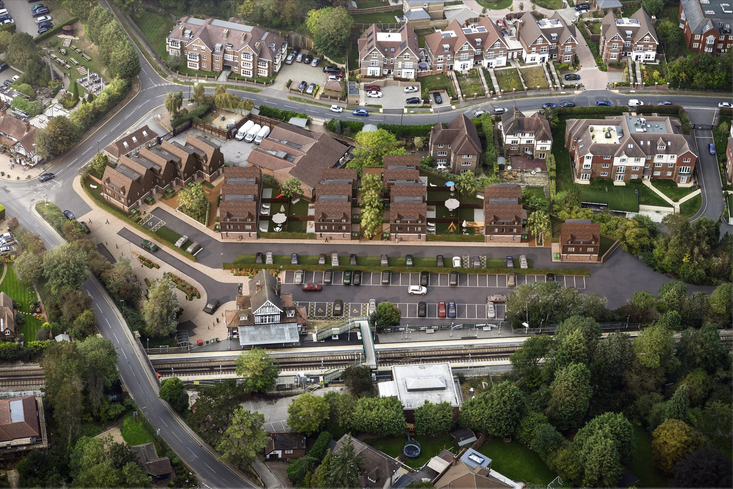 An aerial view of a residential area with houses, a parking lot, a railway track, and surrounding greenery.