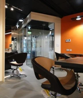 Modern office space with glass-walled meeting room, black desk chairs, and orange accent walls.