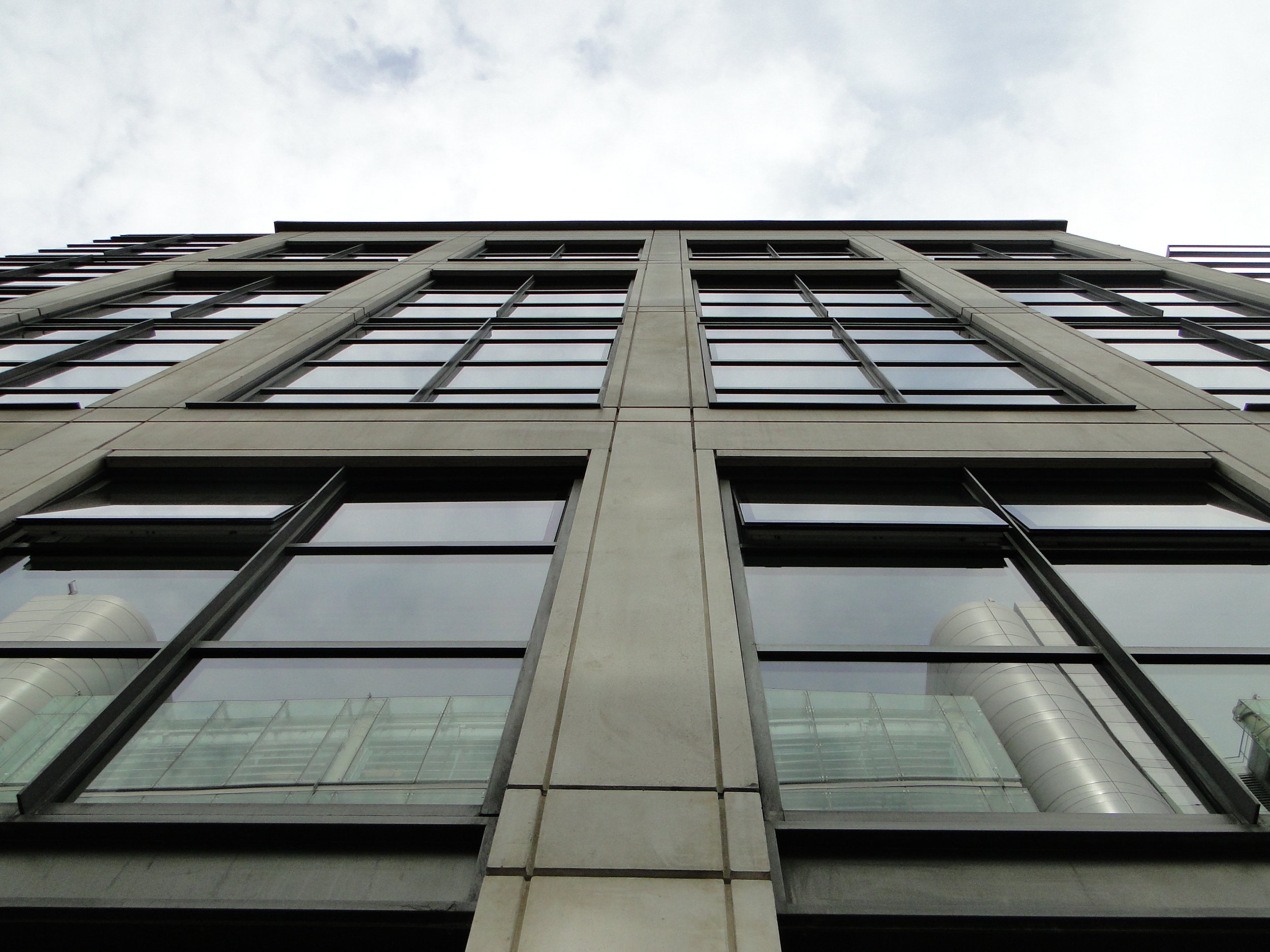 Low-angle view of a modern glass and concrete building against cloudy sky.