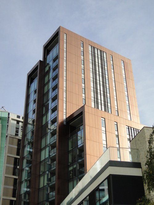Modern multi-story apartment building made of brick and glass with a geometric design and windows, under a blue sky.
