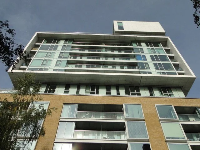 Low-angle view of a modern multi-story building with glass windows and balconies, against a clear blue sky.