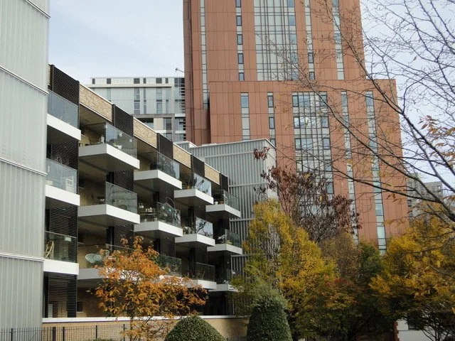 Modern apartment building with balconies and glass railing, surrounded by autumn trees in an urban setting.
