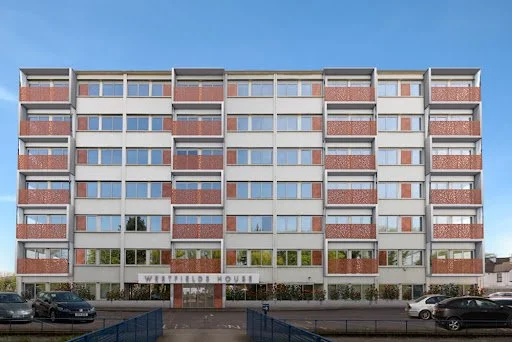 Front view of a multi-story brick and glass apartment building under a clear blue sky.