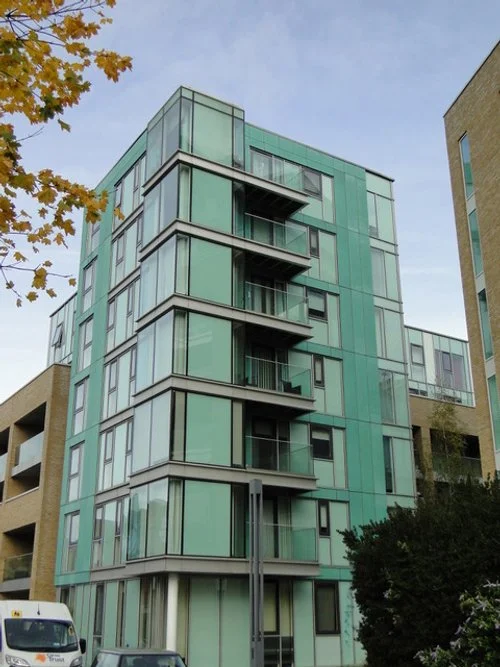 A modern multi-story building with green-tinted glass exterior and small balconies.