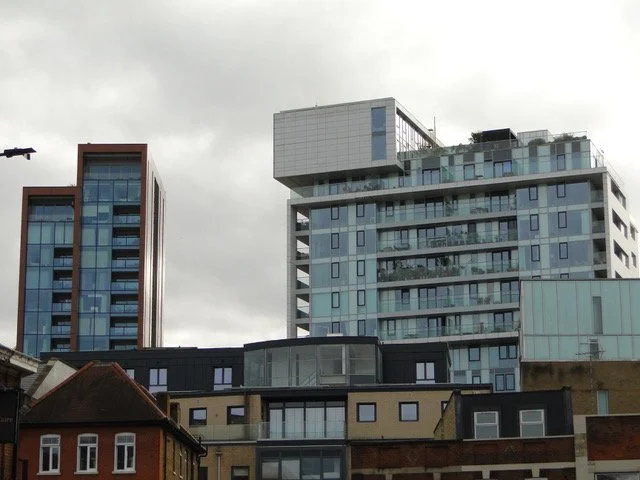 Cityscape featuring modern high-rise buildings with glass facades and older brick buildings in the foreground under a cloudy sky.