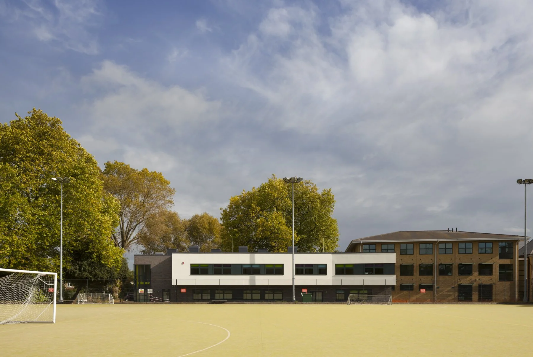 An outdoor sports field with goal posts, surrounded by trees and buildings, under a partly cloudy sky.