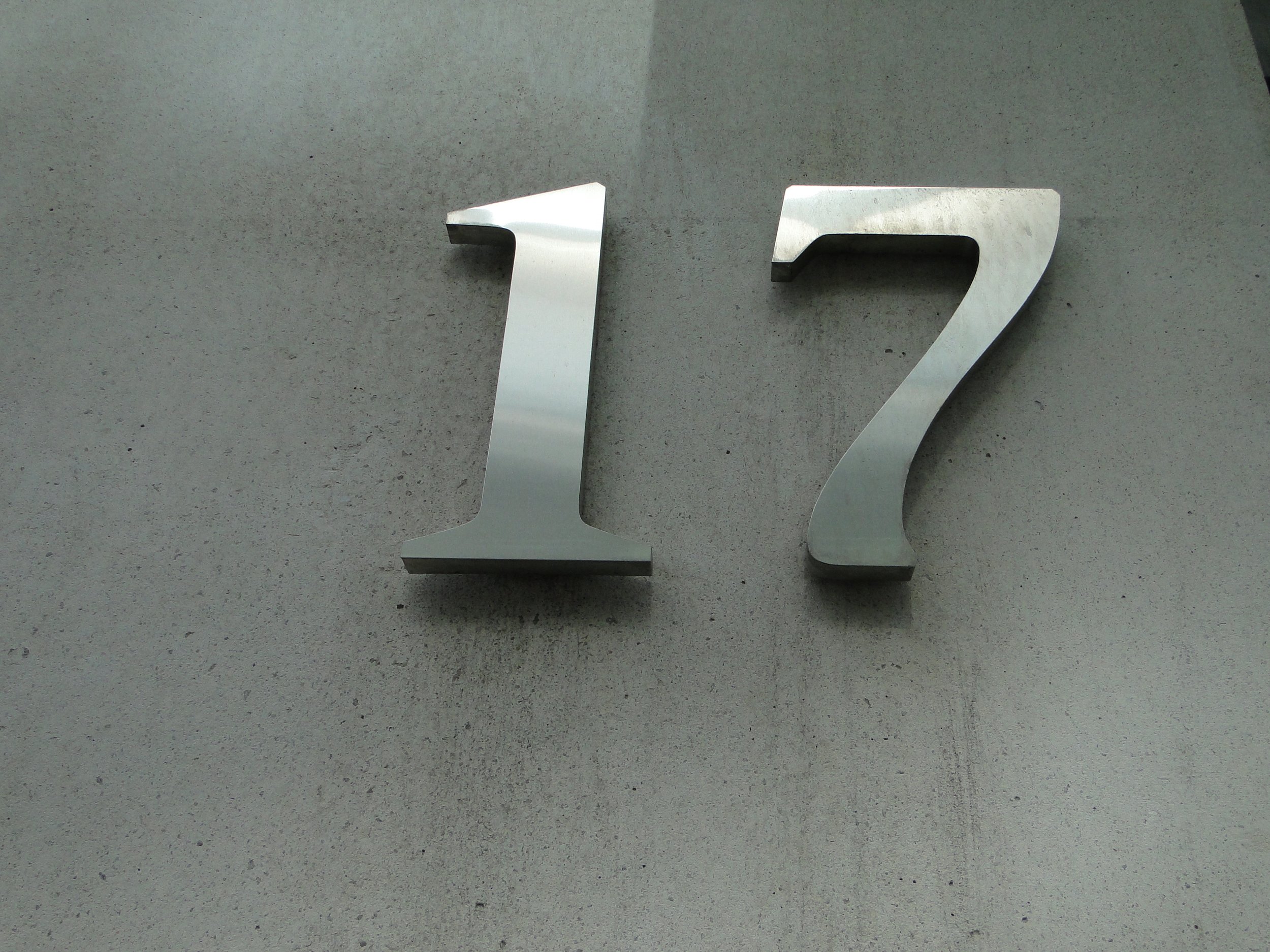 Metal number '12' mounted on a gray concrete wall.