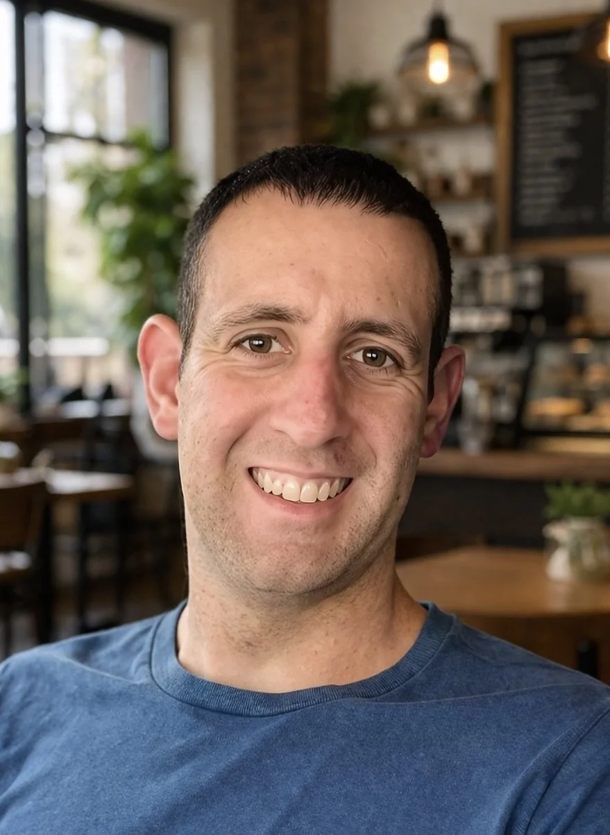A man with short dark hair and a blue T-shirt smiling in a close-up photo.