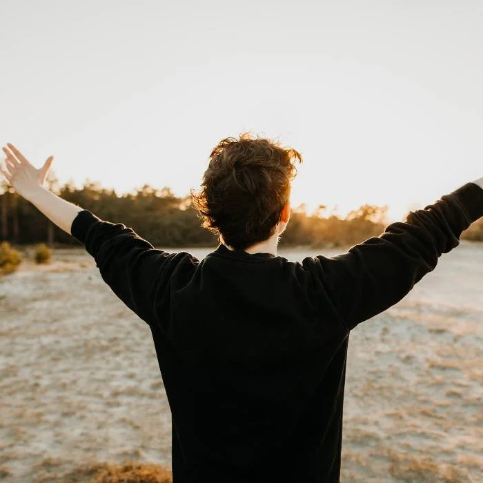 Man standing on a beach with arms out towards the sun.