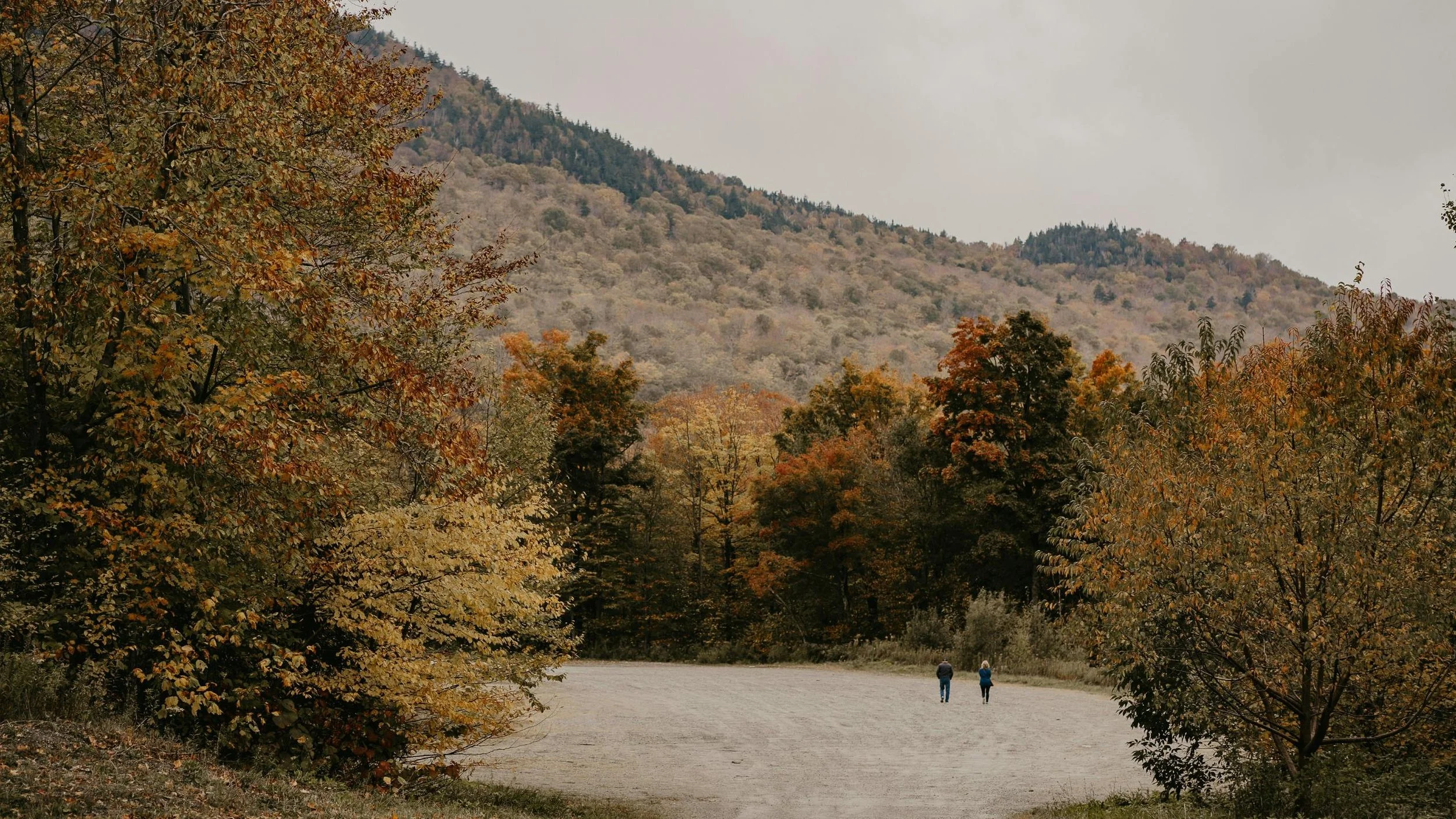 Man and woman walking down dirt road in late fall.