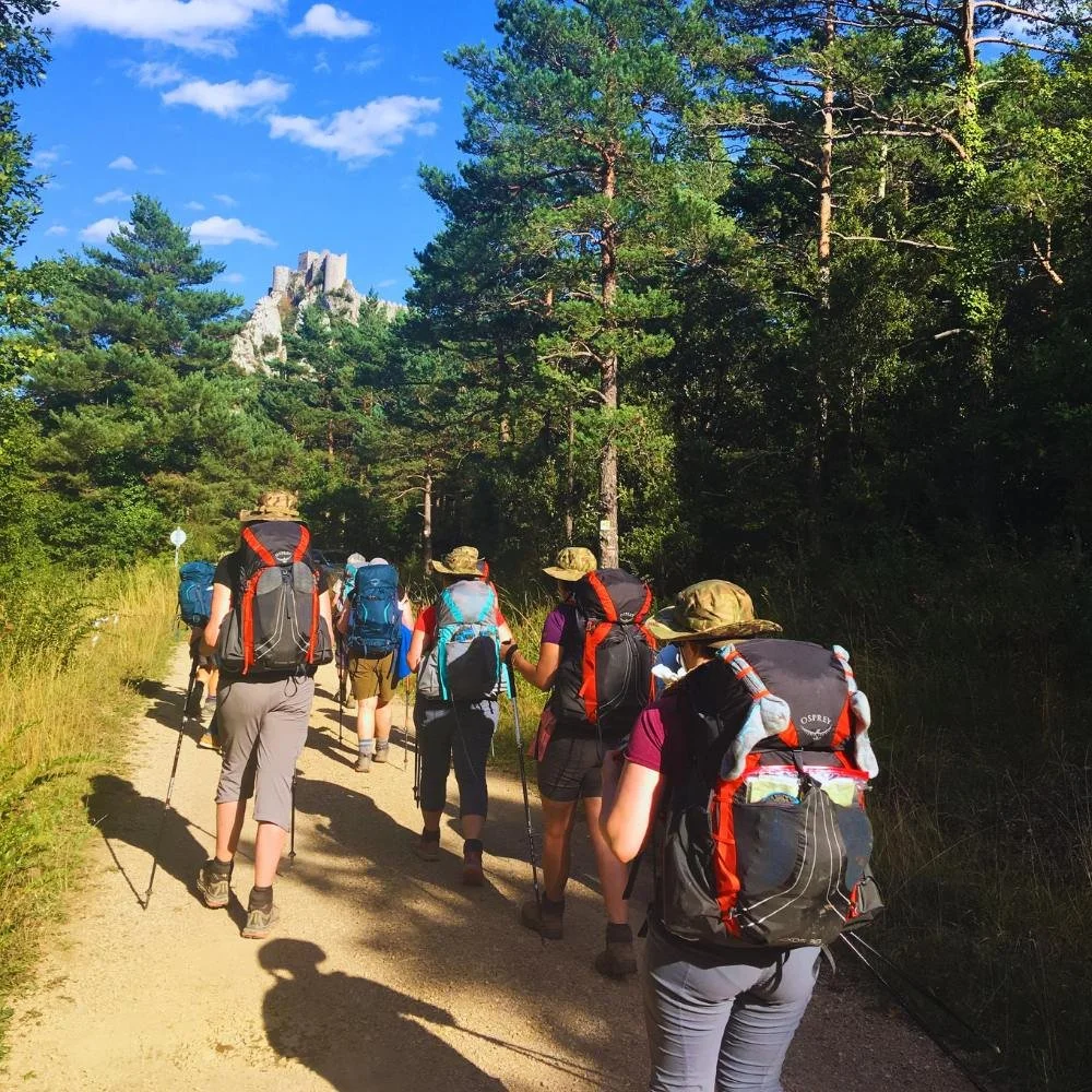 Female hikers wearing large backpacks and walking towards a castle.
