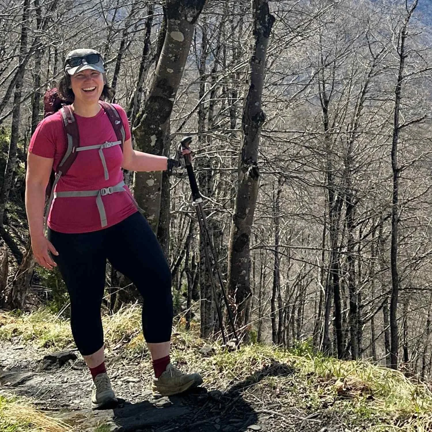 Anna hiking on a wooded mountain trail with trekking poles and backpack during an Athara retreat in Europe.