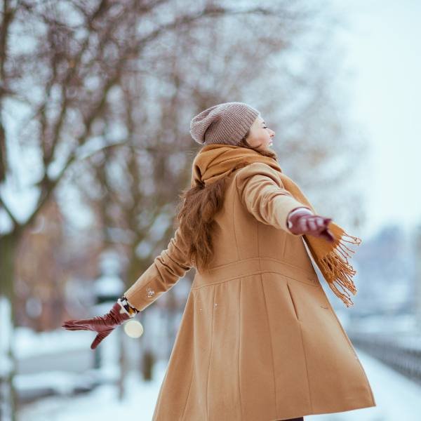 Young woman laughing with arms out on the sidewalk in winter.