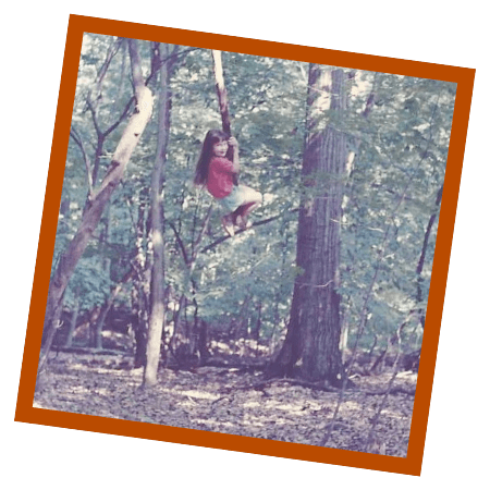 Anna as a child climbing a tree in a wooded area.