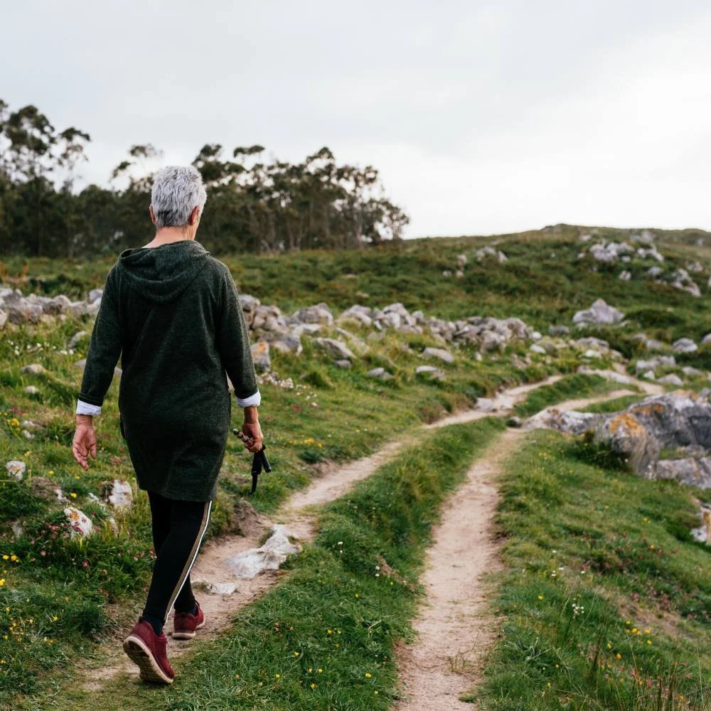 Woman in her 70s walking on a trail with green grass