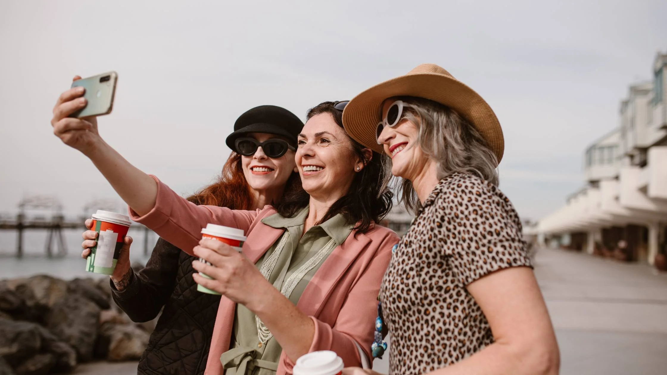 Three midlife women holding coffees and taking a selfie.