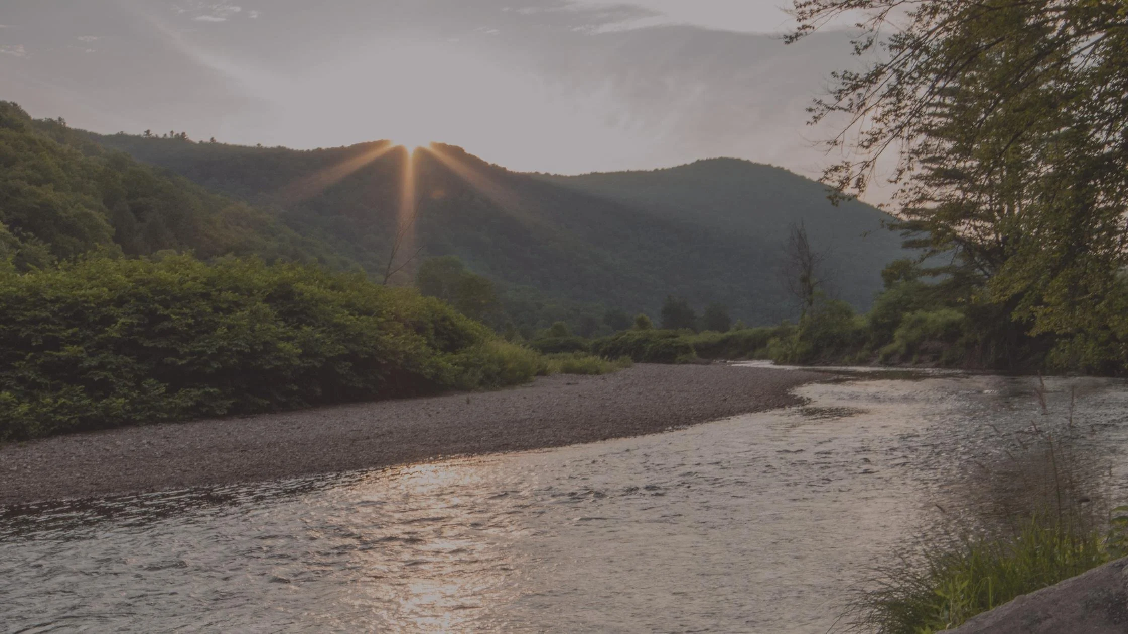 River with green bushes and mountains in the background and the setting sun.