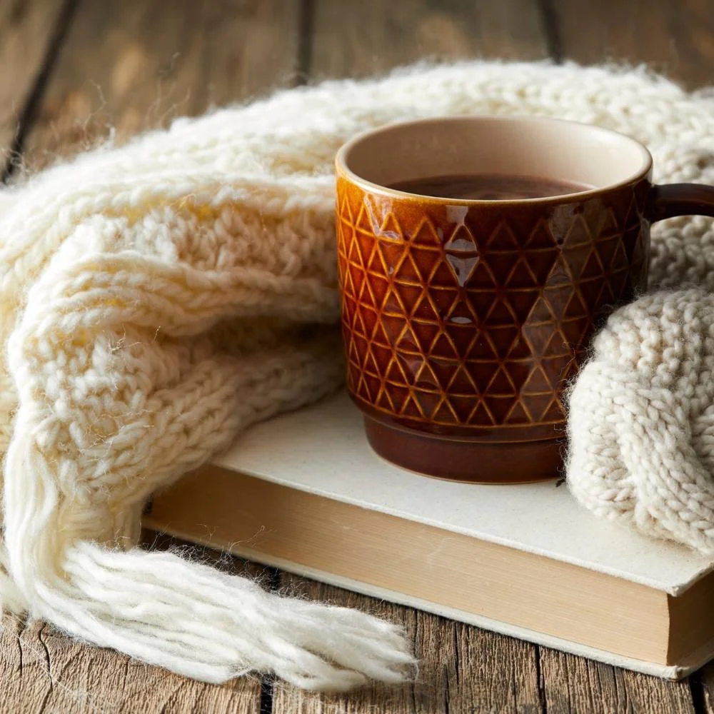 Book, white woven blanket, and a mug of coffee