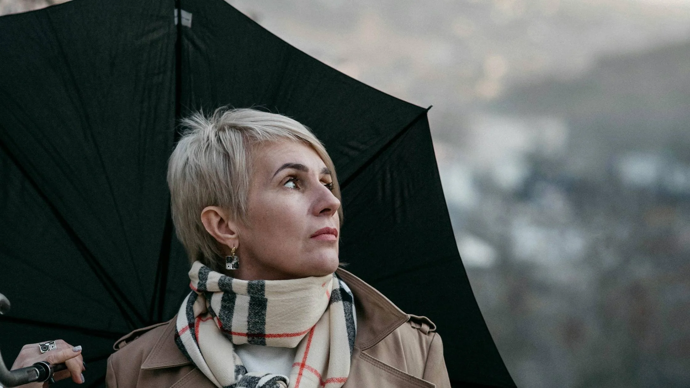 Midlife woman in her 40s with an umbrella looking at the sky.