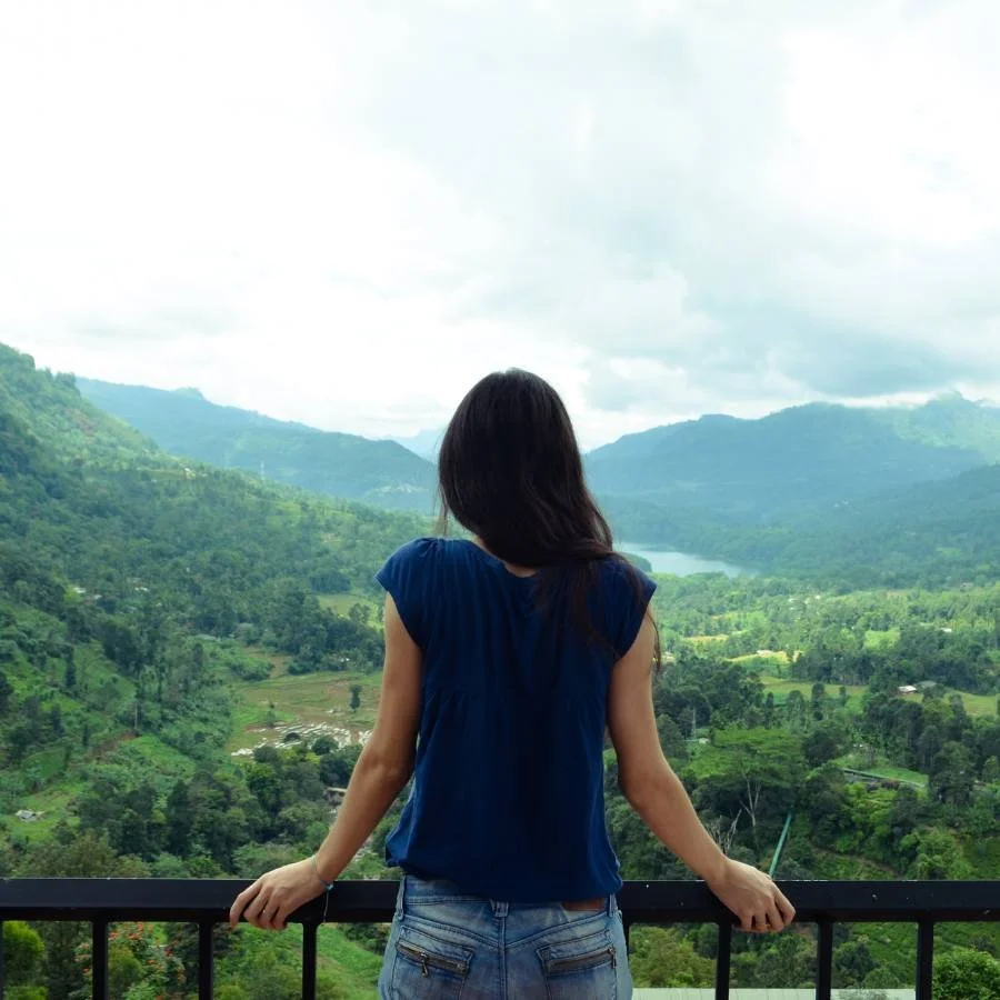 woman standing on balcony looking over green rolling hills
