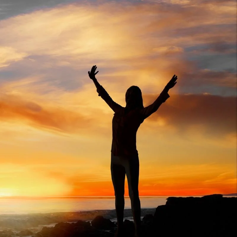 Woman with outstretched arms facing the sunset.