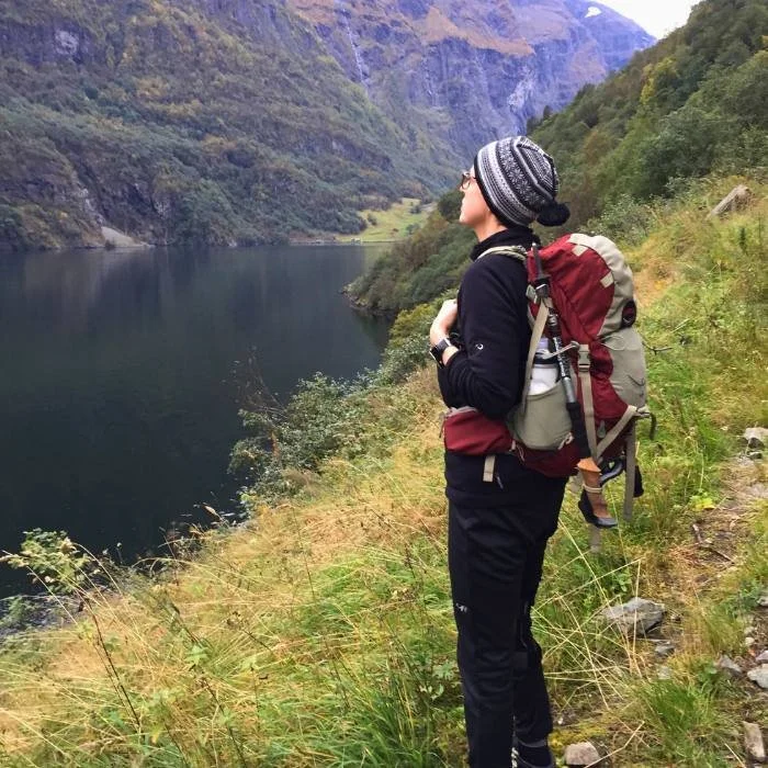 Midlife woman looking over a fjord, wearing a hiking backpack.