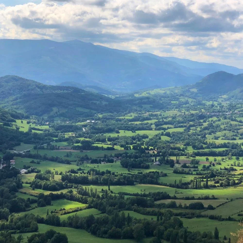 Sun streaming onto a green valley with mountains in the background.