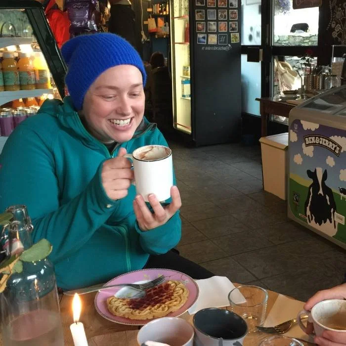 Smiling woman drinking hot chocolate and eating a waffle.