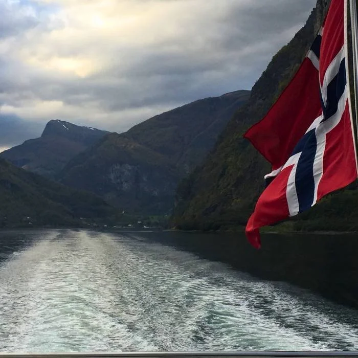 Norwegian flag flying behind a boat traveling in a fjord.