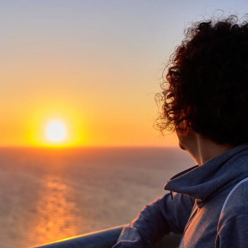 Midlife woman looking over water at the sunset.