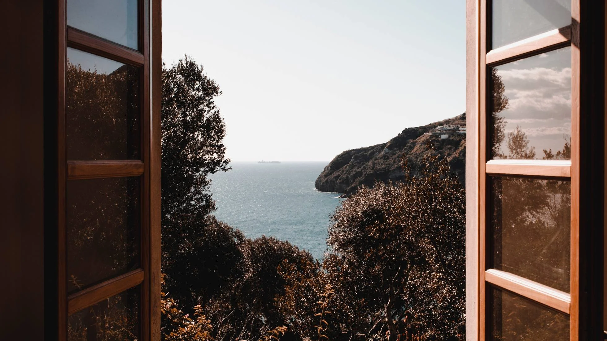 View out an open window onto the sea on a sunny but hazy day.