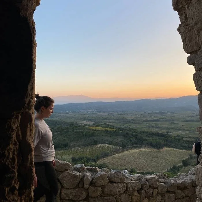 Woman walking past open stone doorway with sunset in the background.