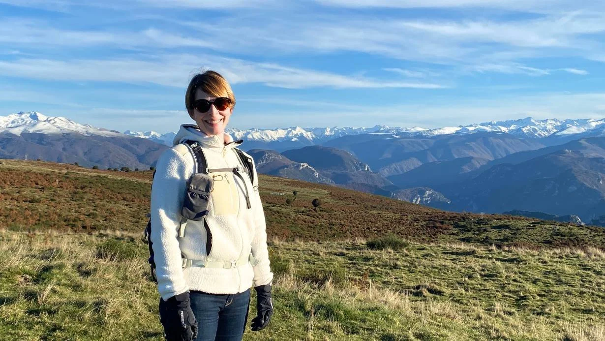 Seoka Salstrom, PhD, standing on a mountain with the snowy French Pyrenees Mountains in the background.